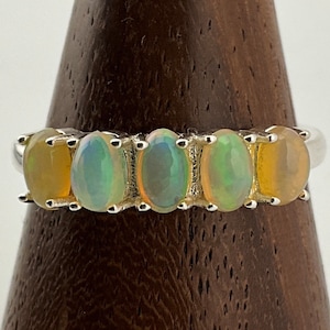 Könnte beinhalten: Ein Silberring mit fünf ovalen Opalen. Die Opale sind eine Mischung aus Weiß, Grün und Gelb.