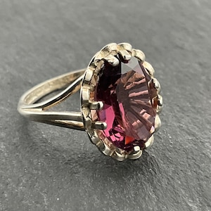 May include: A silver ring with a large, faceted, purple gemstone set in a scalloped bezel.