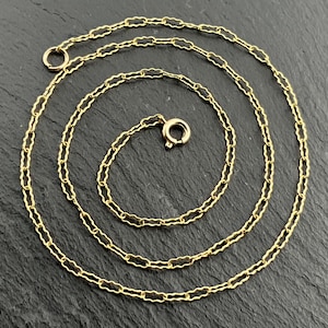 May include: A gold-toned chain necklace featuring a series of elongated, scalloped-edge oval links connected in a continuous pattern. The necklace includes a circular spring ring clasp at one end and a small jump ring at the other end.