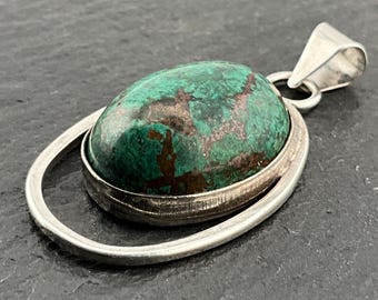 May include: A silver pendant with a green oval gemstone set in a silver bezel. The pendant has a simple, modern design.
