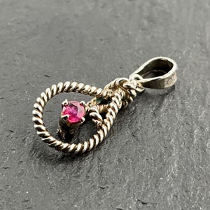 May include: A silver pendant featuring a pink gemstone set within a twisted rope design.