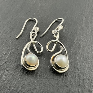 Pode incluir: Um par de brincos de prata com uma pérola branca e um design de espiral.
