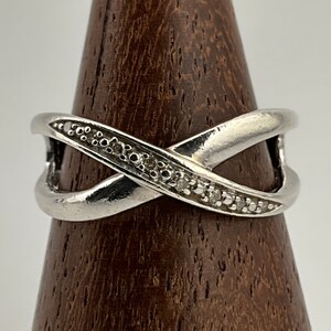 May include: A silver ring with a criss-cross design and a row of small diamonds.