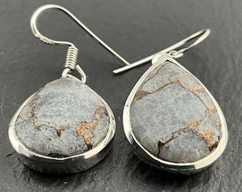 May include: A pair of silver teardrop earrings. Each earring features a gray stone with copper-colored veining, set in a silver bezel. The earrings have a simple hook design for pierced ears. The stones have a natural, organic appearance.