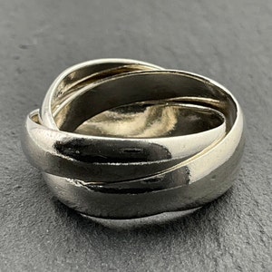 Op de afbeelding: Een zilveren ring met drie in elkaar grijpende banden. De ring is glad en gepolijst.