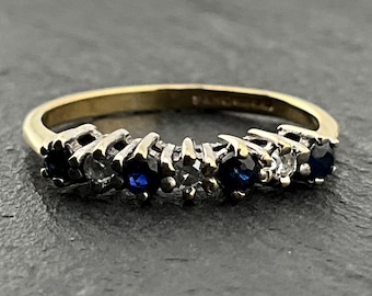 May include: A gold ring featuring a line of alternating blue and clear gemstones. The ring has a slender gold band, and the gemstones are set in a silver-coloured metal.