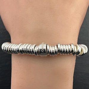 May include: A silver bracelet with multiple stacked rings, featuring a charm with the inscription "S LONDON".