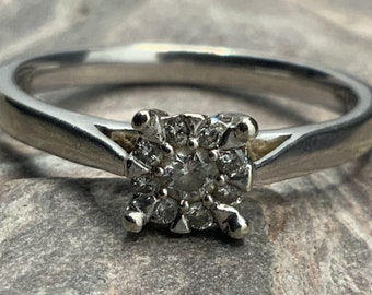 Puede incluir: Un anillo de plata con un grupo de pequeños diamantes engastados en forma cuadrada.