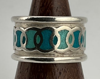 Puede incluir: Un anillo de plata con una banda de esmalte turquesa y azul verdoso. El esmalte está en un patrón geométrico de círculos y óvalos.