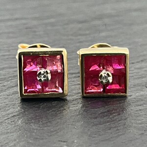 May include: A pair of square stud earrings featuring four princess-cut red rubies arranged in a grid pattern. Each earring is set in a gold frame and includes a single, small, round, clear diamond centred at the intersection of the four rubies.