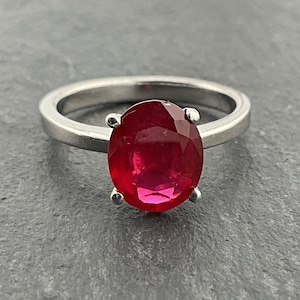 Könnte beinhalten: Ein silberner Ring mit einem großen, ovalen Rubin-Edelstein, der in einer Krappenfassung sitzt.