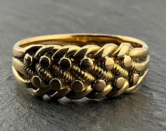 Könnte beinhalten: Ein goldfarbener Ring mit einem komplexen geflochtenen Design. Das Band besteht aus mehreren ineinander verschlungenen Strängen mit einer mittleren Reihe aus kleinen, glatten, kreisförmigen Metallperlen und strukturierten, gerippten Segmenten.