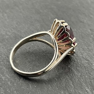 May include: A silver ring with a large, faceted, purple gemstone set in a decorative, scalloped halo.