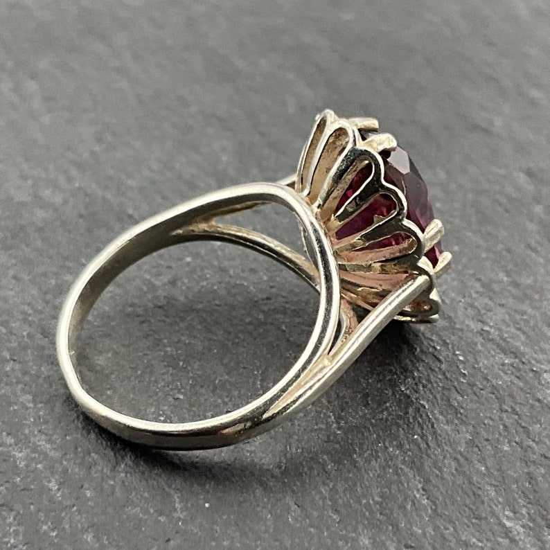May include: A silver ring with a large, faceted, purple gemstone set in a decorative, scalloped halo.
