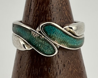 Puede incluir: Un anillo de plata con un diseño de esmalte verde. El anillo está hecho de dos bandas que están entrelazadas y tienen una forma ondulada. El esmalte es de color verde claro y tiene un acabado texturizado.