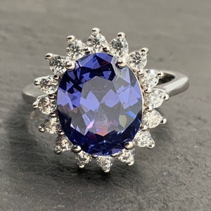 May include: A silver ring featuring a large oval purple gemstone encircled by a halo of smaller clear gemstones.