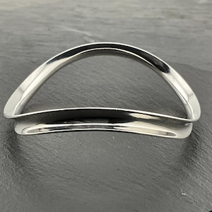 May include: A silver bangle bracelet with a curved, wave-like design.