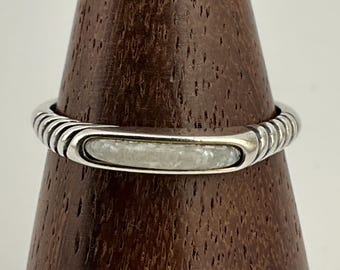 May include: A silver ring featuring a rectangular, iridescent, light-coloured stone. The band has a ribbed design on the sides. The ring is displayed on a wooden stand.