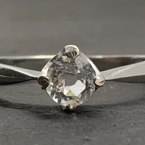 May include: A silver ring with a clear, round gemstone set in a simple, four-prong setting.