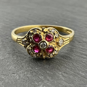 Könnte beinhalten: Ein goldener Ring mit einem blütenförmigen Design, das fünf rote Rubine und kleinere weiße Diamanten zeigt.