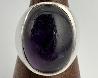 May include: A silver ring with a large, oval-shaped amethyst gemstone. The ring has a simple, modern design.