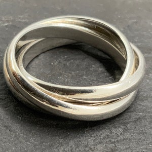 May include: A silver three-band interlocking ring. The ring is made of smooth, polished metal and has a simple, elegant design.