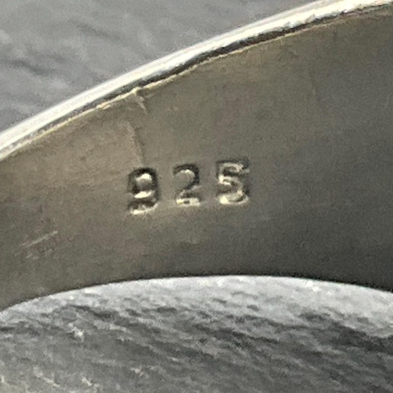 May include: Close-up of a silver ring with the number "925" stamped on the inside band.