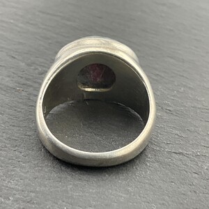 May include: A silver ring with a large, oval-shaped, dark pink gemstone set in the center.