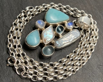 May include: A silver chain necklace with a pendant featuring a cluster of blue and white gemstones. The pendant is made of silver and features a variety of shapes and sizes of gemstones.