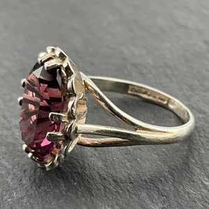May include: A silver ring with a large, faceted, purple gemstone set in a decorative, silver setting.