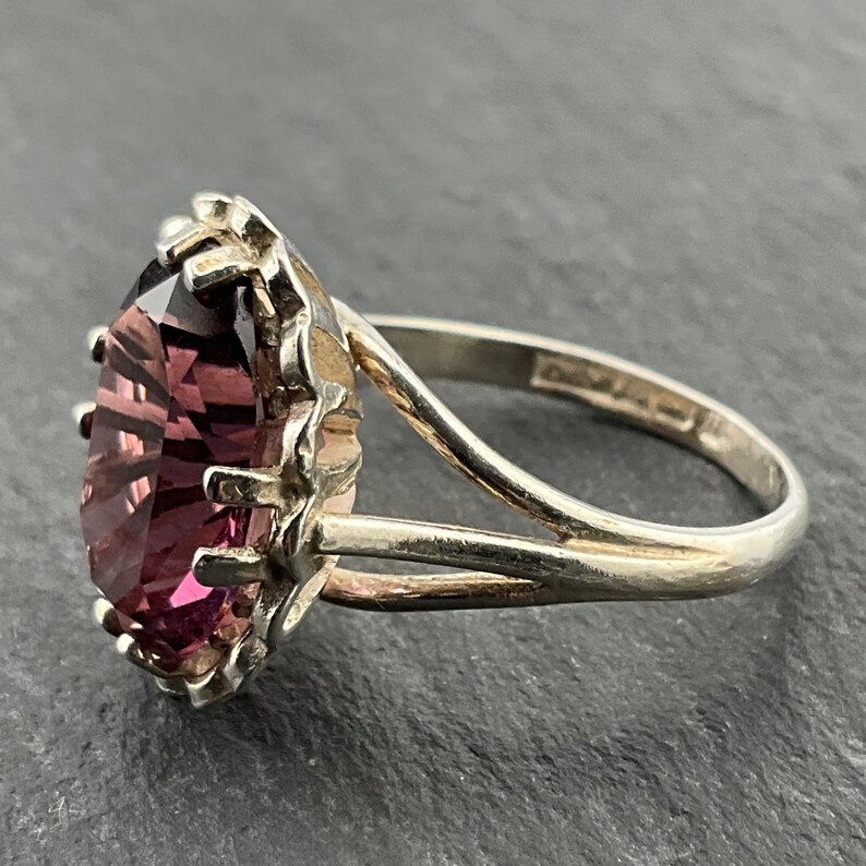 May include: A silver ring with a large, faceted, purple gemstone set in a decorative, silver setting.