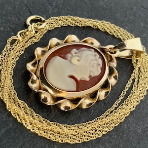May include: A gold chain necklace with a cameo pendant. The cameo is a portrait of a woman's face carved in shell and set in a gold frame.