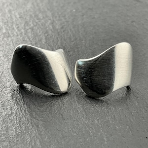 May include: A pair of silver earrings with a brushed finish. The earrings are shaped like a wave and have a modern, abstract design.
