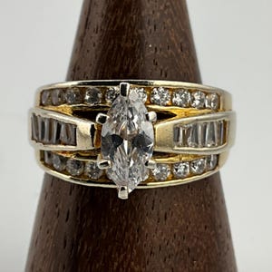 May include: A gold ring featuring a large marquise-shaped diamond surrounded by smaller diamonds. The ring has a band with multiple rows of smaller diamonds.