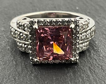 May include: A silver ring with a large square pink gemstone surrounded by a halo of smaller clear gemstones.