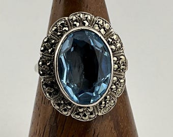 Puede incluir: Un anillo de plata con una gran piedra ovalada azul rodeada de un diseño detallado de piedras de marcasita.
