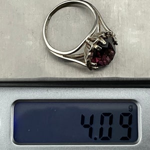 May include: A silver ring with a large, dark purple gemstone set in a crown-like design. The ring weighs 4.09 grams.