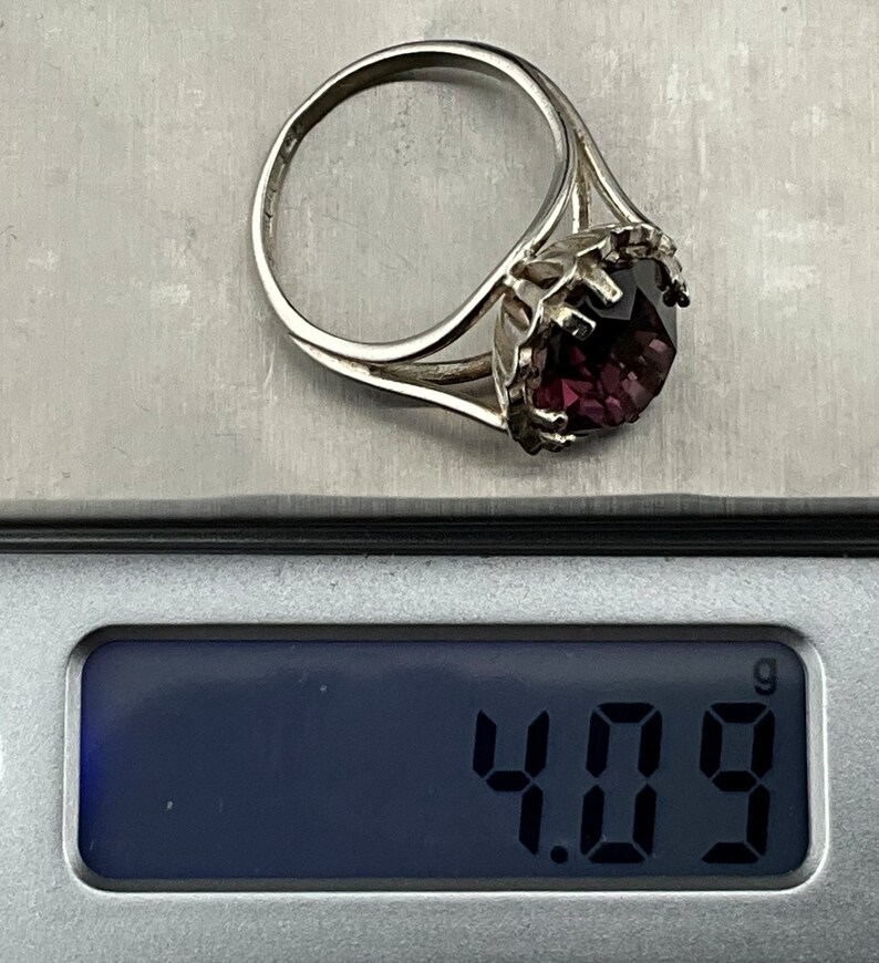 May include: A silver ring with a large, dark purple gemstone set in a crown-like design. The ring weighs 4.09 grams.