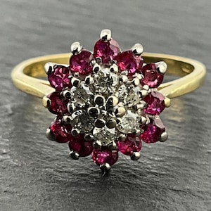 Puede incluir: Un anillo de oro con un racimo de rubíes rojos y diamantes blancos engastados en forma de flor.