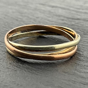 May include: A tri-color interlocking ring featuring three thin, smooth bands in yellow, rose, and white gold tones. The three circular bands are linked together in a continuous, overlapping design, creating a polished and reflective metallic surface.