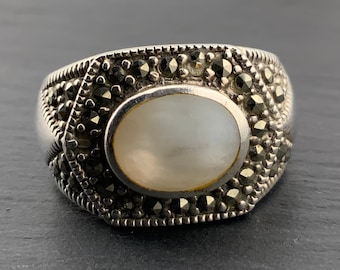 May include: A silver ring with a white oval gemstone surrounded by black marcasite stones.