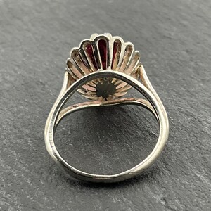 May include: A silver ring with a red and white flower design. The ring is set with a single red stone in the center of the flower.