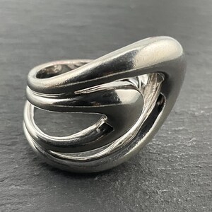 Puede incluir: Un anillo de plata con un diseño abstracto único. El anillo está hecho de múltiples bandas que están entrelazadas y retorcidas.