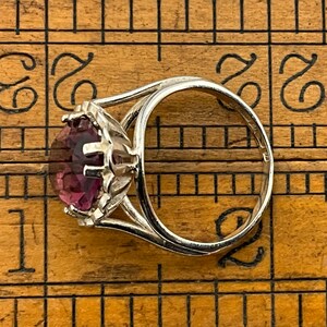 May include: A silver ring with a large, round, purple gemstone set in a prong setting. The ring is on a wooden ruler.