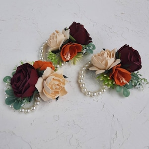 May include: Three pearl bracelets with burgundy, peach, and orange silk flowers. The bracelets are perfect for a wedding or special occasion.