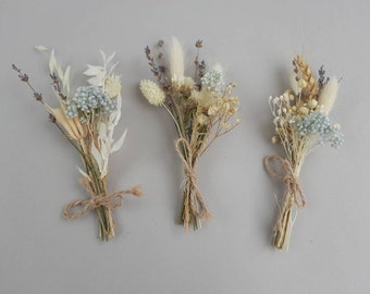 May include: Three small bouquets of dried flowers tied with brown twine. Each bundle features a mix of light blue, cream, and beige botanical elements, including sprigs of lavender, fluffy bunny tails, and delicate white foliage stems.