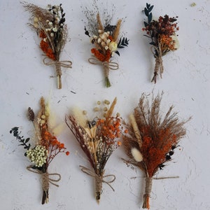 May include: Six dried flower bouquets featuring a mix of orange, white and brown tones. The bouquets are tied with twine and displayed on a white surface.