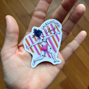 May include: A sticker with a cartoon illustration of a person in a pink swimsuit, decorated with stars, in a dynamic pose. The background has orange and white stripes, and the sticker has the text "SALBSCHTLI&Auml;BI Club".
