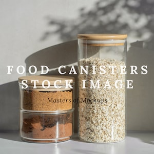 Op de afbeelding: Drie glazen voedselcontainers met houten deksels. Eén hoge container is gevuld met havermout en twee kleinere containers bevatten bruine suiker en cacaopoeder. De tekst "FOOD CANISTERS STOCK IMAGE" wordt weergegeven.