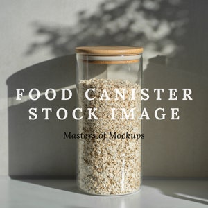 Op de afbeelding: Een heldere glazen voedselcontainer gevuld met haver, afgedekt met een houten deksel. De tekst "FOOD CANISTER STOCK IMAGE" staat erop. De afbeelding staat tegen een neutrale achtergrond met schaduwen.